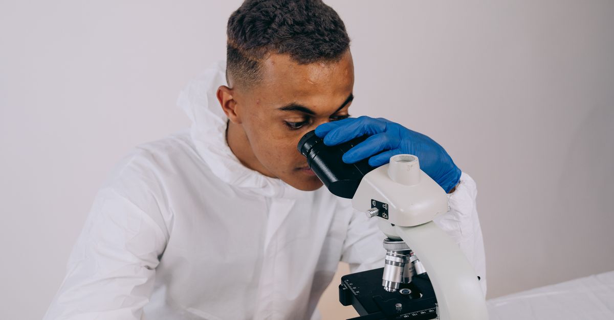 A researcher in protective gear using a microscope for scientific study.