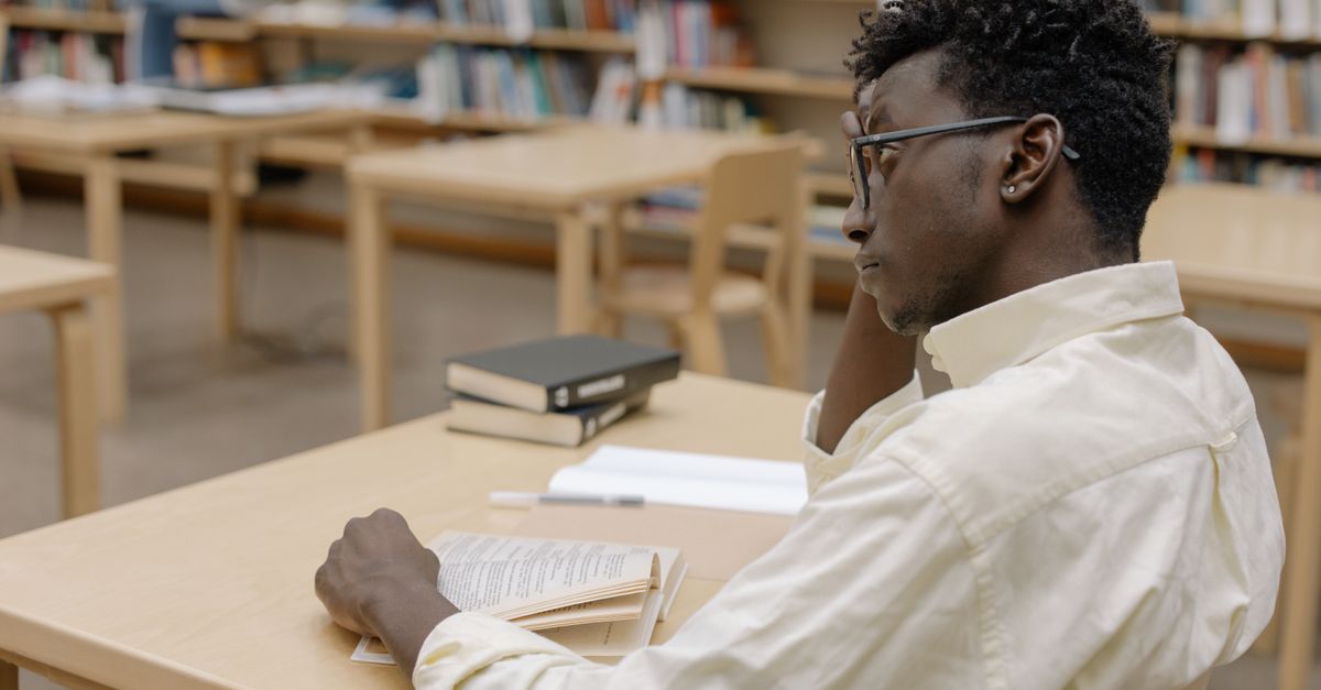 Young adult studying intently in a library with books and empty desks around.